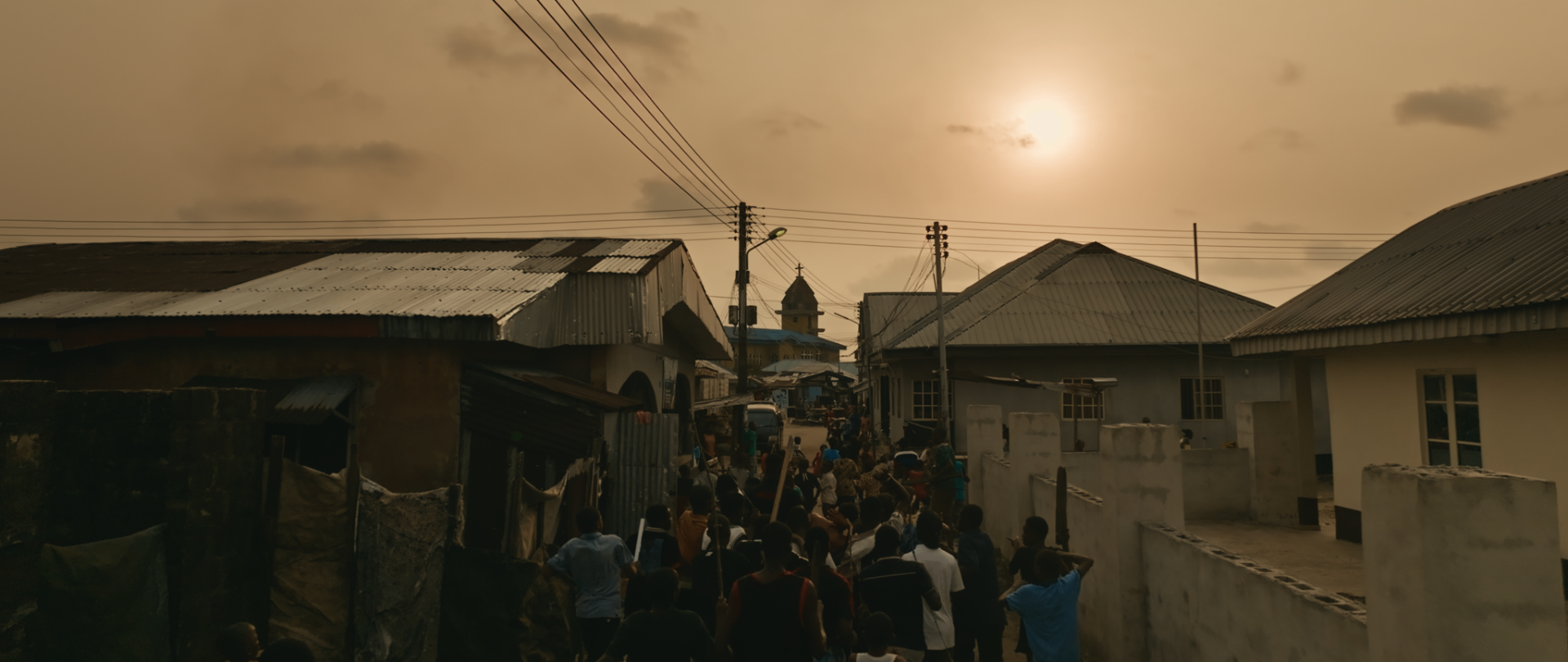 A crowd marches through the village at sunset